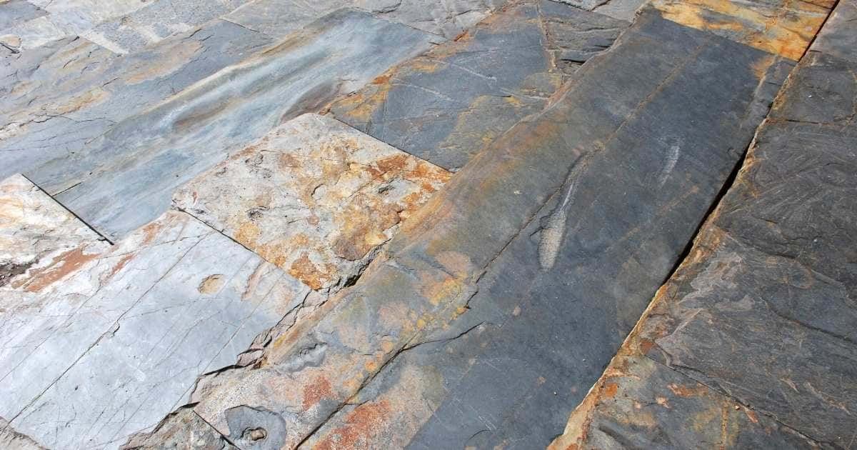 Een vloer bekleed met grote, blauwgrijze leistenen met roestkleurige vlekken.