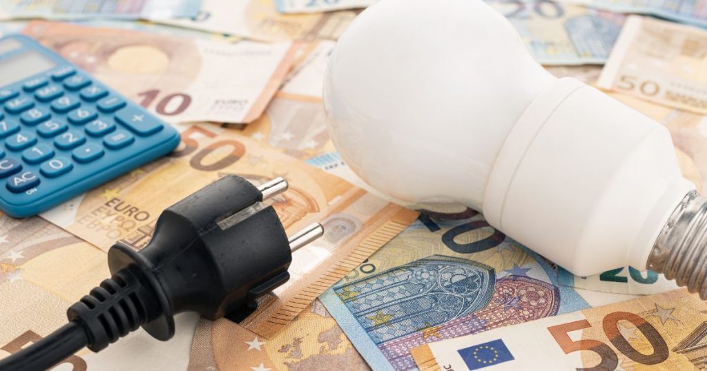 Een spaarlamp, stekker en rekenmachine bovenop een stapel biljetten van 10, 20 en 50 euro.