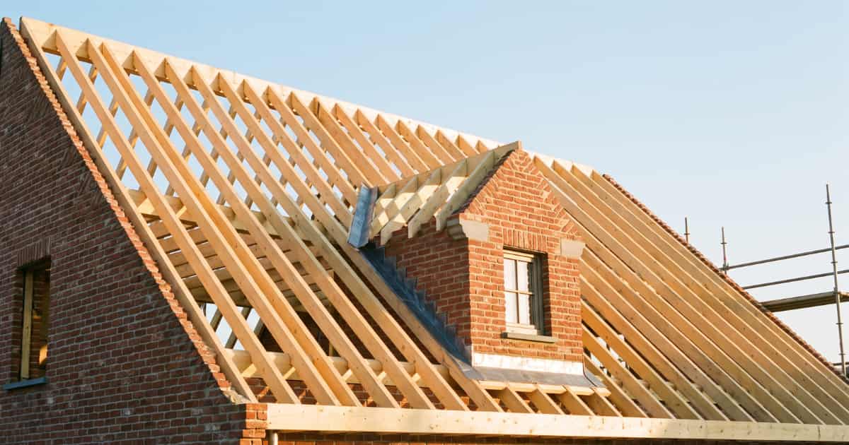 Houten dakconstructie in opbouw op een bakstenen woning met evenwijdig geplaatste kepers die van de nokbalk naar de muurplaat lopen en een gemetselde dakkapel met klein raam zichtbaar tussen de spanten.