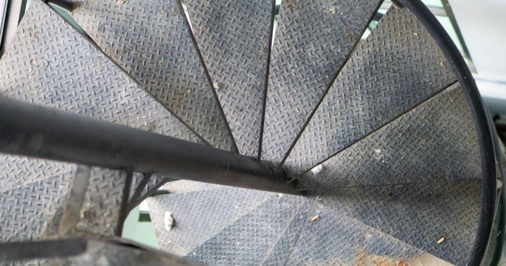 Detail van een metalen wenteltrap die beneden uitkomt op een groenachtige vloer.