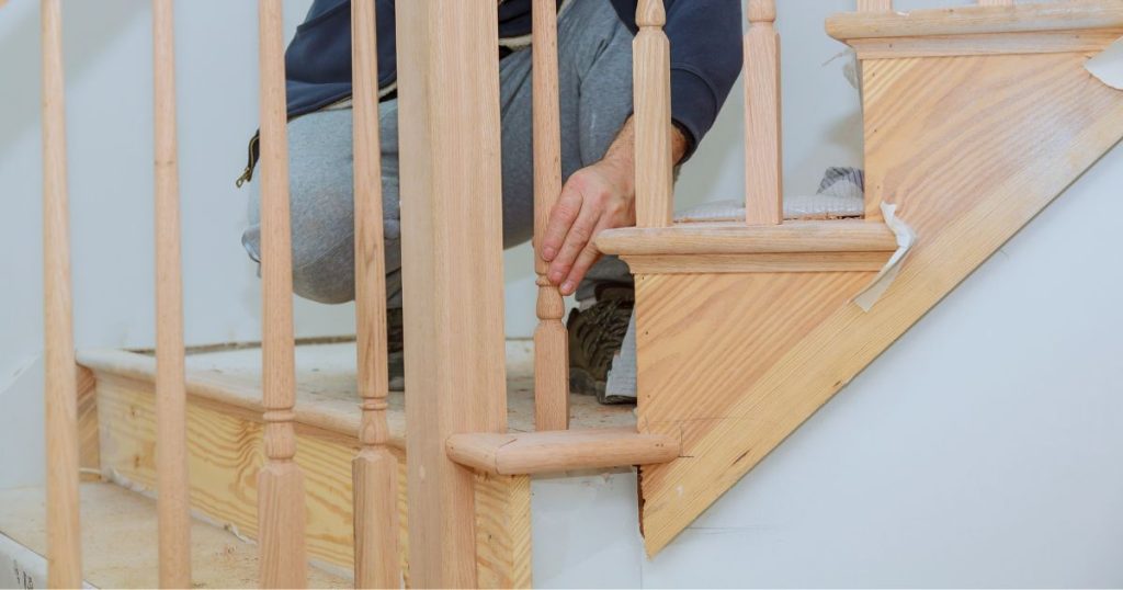 Een vakman bevestigt en controleert de houten spijlen voor de trapleuning op een pas geplaatste houten trap.
