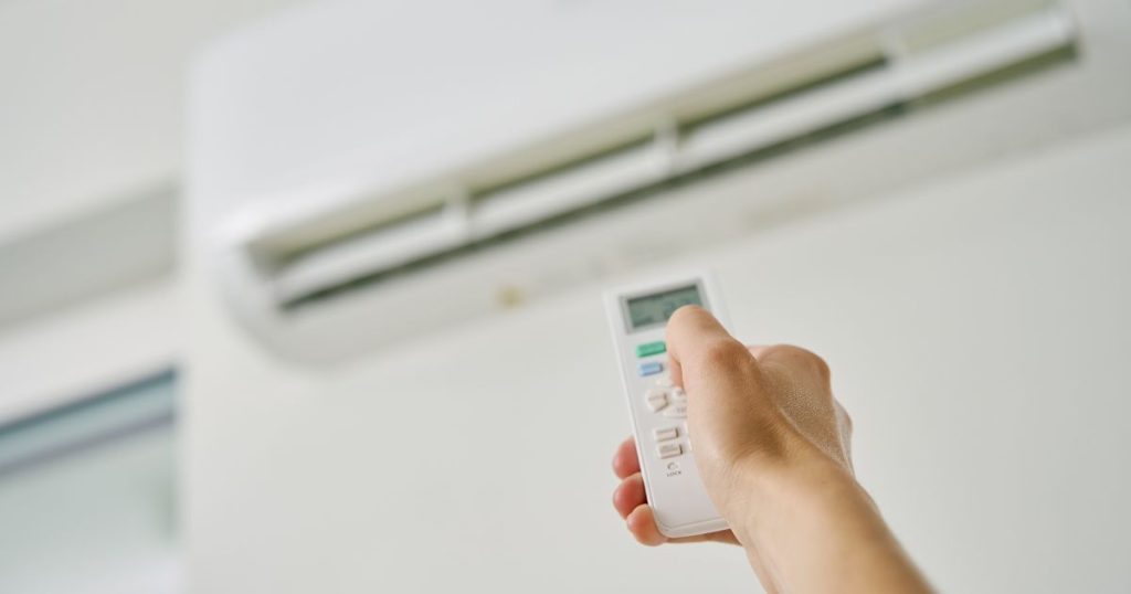 Een afstandsbediening met een scherm van een airconditioning binnenunit in een hand van een man.
