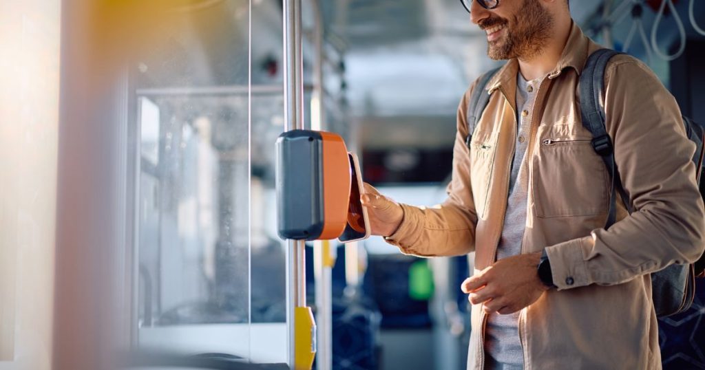 Man met stoppelbaard en bril houdt in de bus zijn smartphone voor een ticket validator.