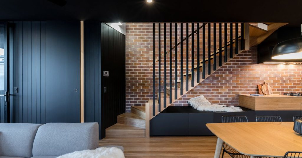 Een houten trap met zwarte metalen leuning in een industrieel interieur. De bewoners lieten de trap opmeten door een expert om te bepalen hoe ze de ruimte onder de trap best konden indelen en benutten. Onder de nieuwe trap ligt een praktische keuken met zithoek.