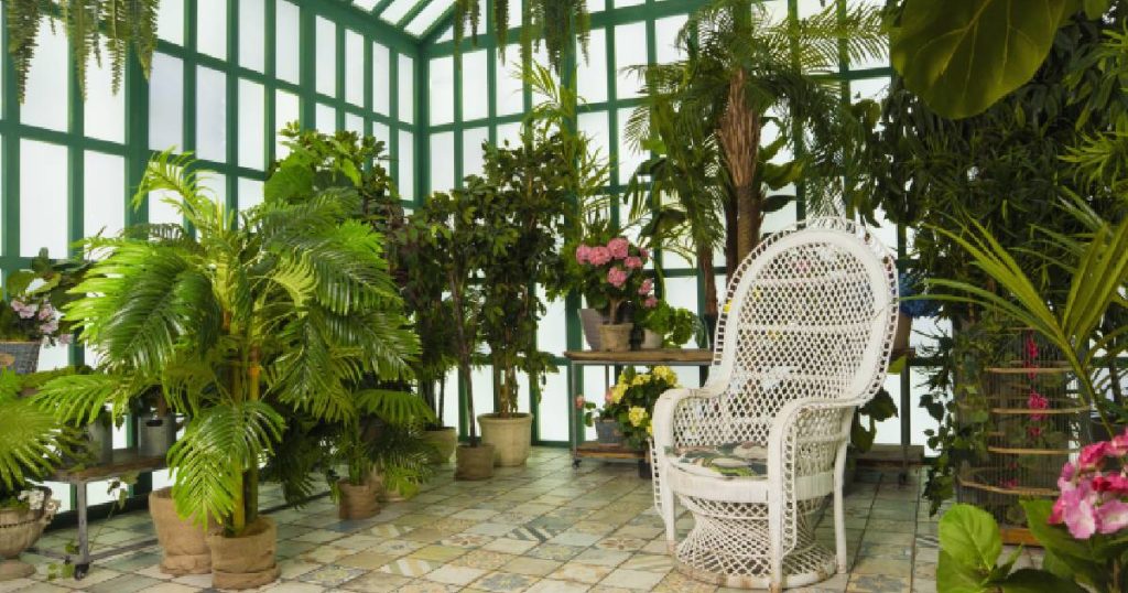 Interieur van een orangerie aanbouw met aluminium raamprofielen. In de orangerie staan verschillende planten en een witte tuinstoel.