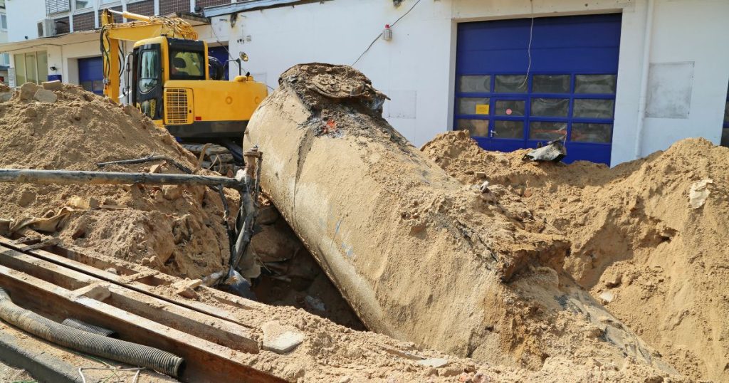 Een kraan in de weer met het uitgraven en verwijderen van een grote ondergrondse mazouttank naast een witte garage met blauwe poort.