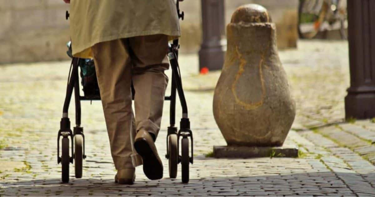 Benen van een persoon met rollator op een weg met kasseien.