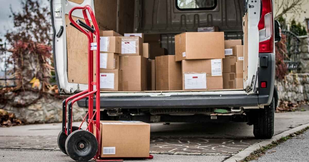 Een open bestelwagen met verschillende gefrankeerde pakketten. Achter de bestelwagen staat een rood karretje met een enkel pakket in kartonnen doos.