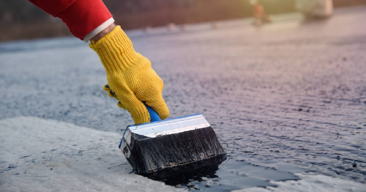 Een dakwerker is druk in de weer met het herstellen van een plat dak met vloeibare rubber of EPDM.