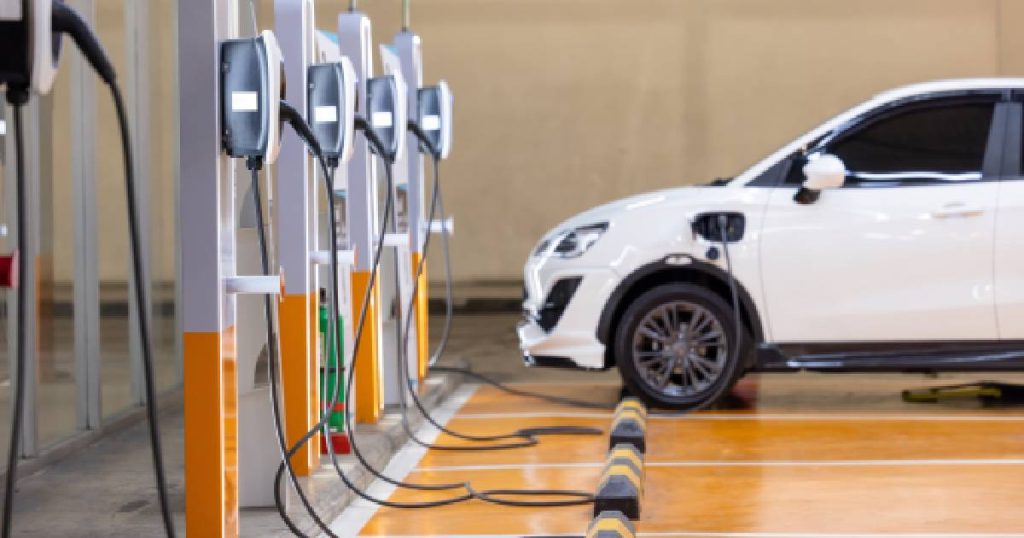 Een parkeerplaats met oranje en grijze laadstations waar een witte auto gekoppeld is aan een van de laders