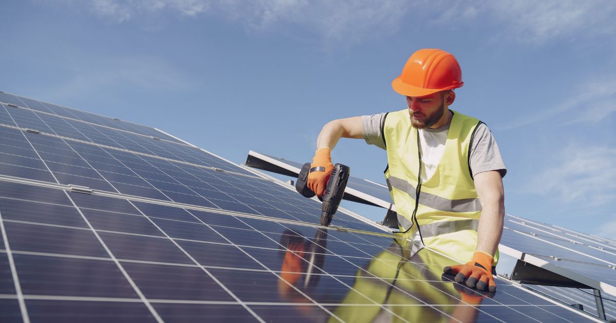 Een zonnepanelen installateur houdt een schroefboor vast om een paneel vast te draaien op een geleider op het onderliggende dak.