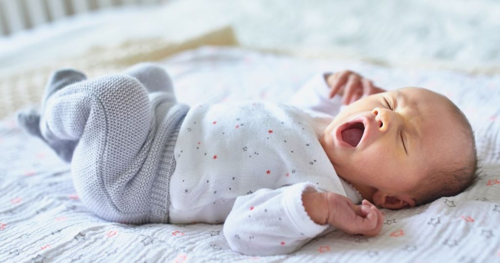 Een pasgeboren baby op een zacht deken. De baby draagt een gespikkeld hansopje en een wollen broek.