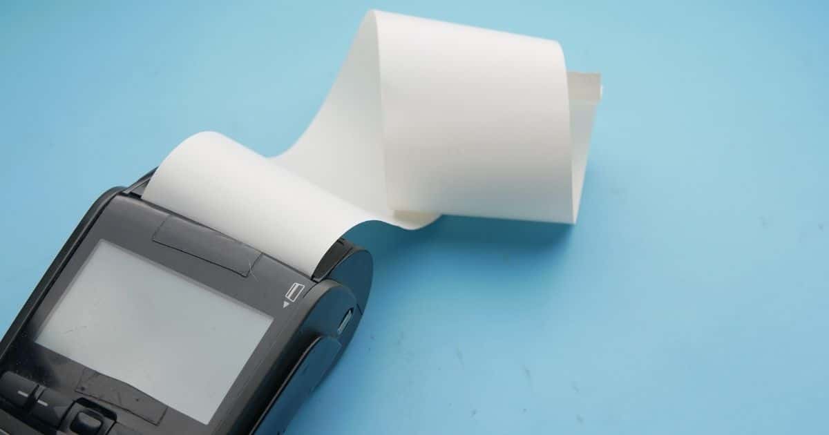 Een betaalterminal met printmodule tegen een lichtblauwe achtergrond. Uit de printmodule komt een lange strook wit papier.