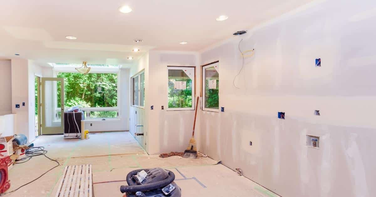 Een gerenoveerde ruimte, afgewerkt met gyprocplaten. Er staan verschillende soorten gereedschap in de ruimte: onder meer een stofzuiger, bezemsteel en kabels.