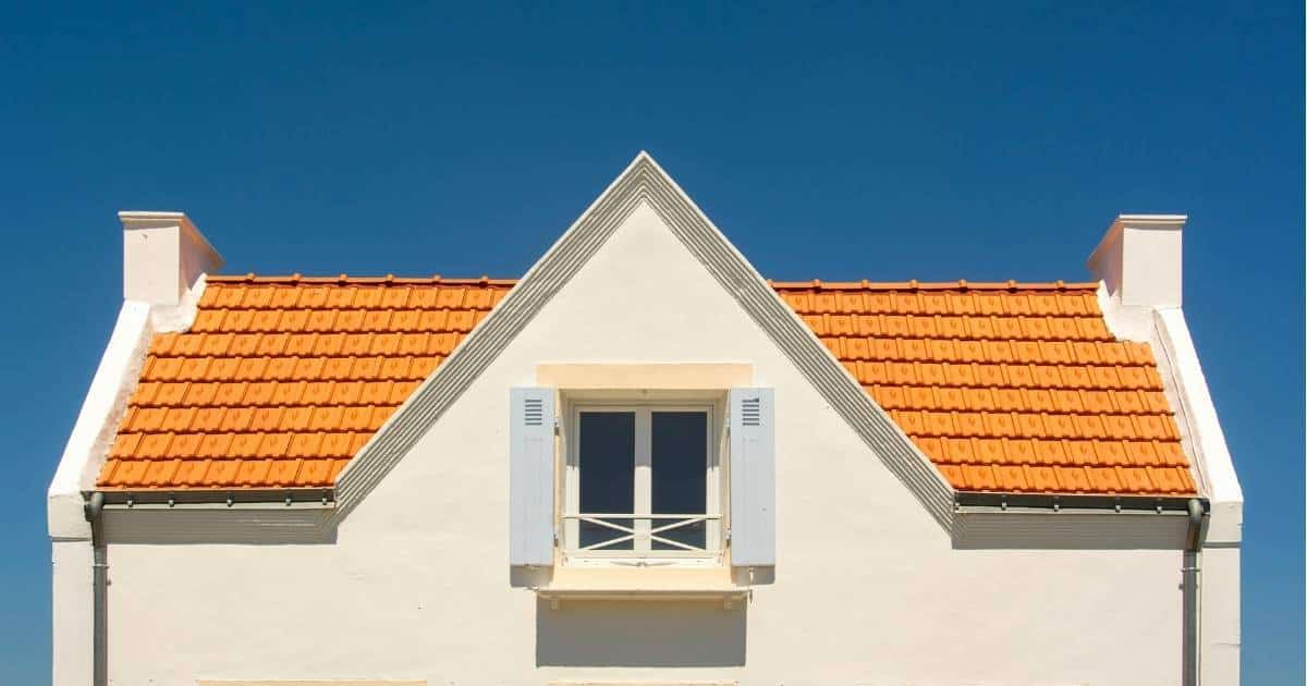 Bovenkant van een woning met witte gevel, hellend dak met oranje dakpannen, en twee schouwen.