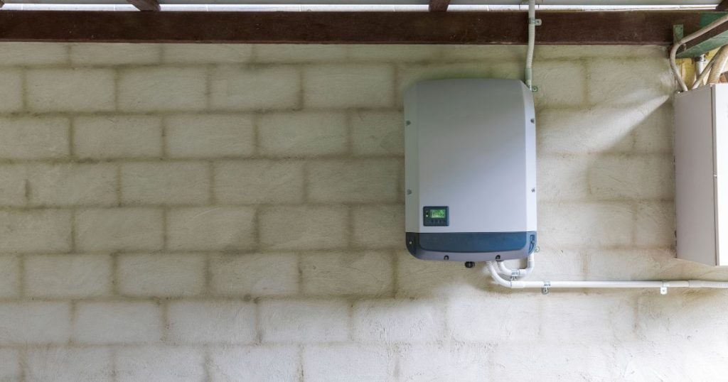 Een kleine thuisbatterij voor zonnepanelen, gemonteerd tegen een witte bakstenen muur.