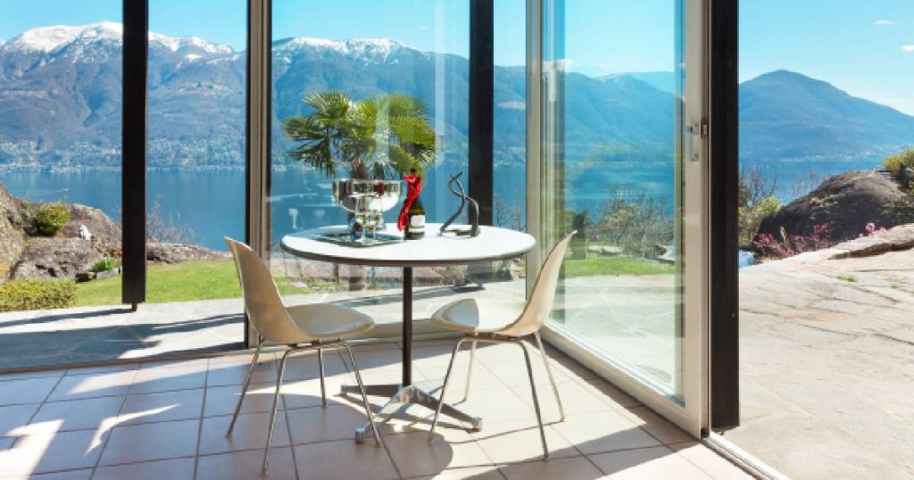 Een Van Der Bauwhede veranda met uitzicht op een berglandschap en meer. In de veranda staat een witte tafel met witte stoeltjes.