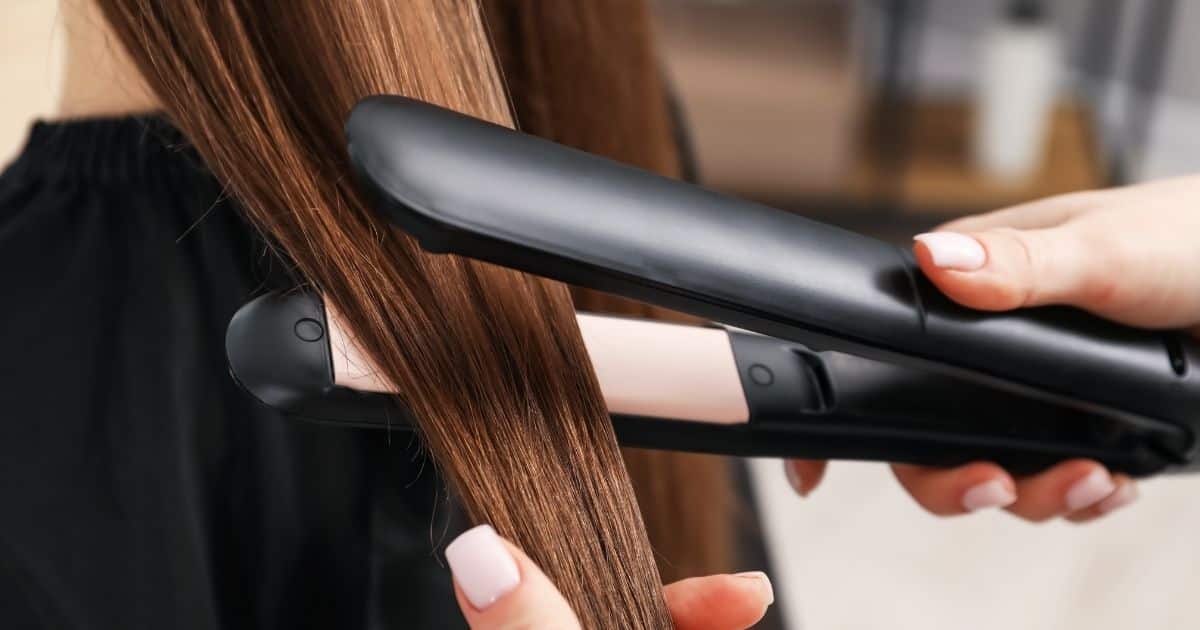 Een kapper of haarstyliste bewerkt het haar van een klant met een stijltang.