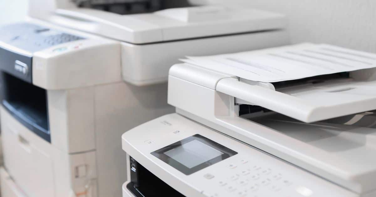 Twee professionele witte kopieermachines (met printer en scanner) tegen een witte muur.