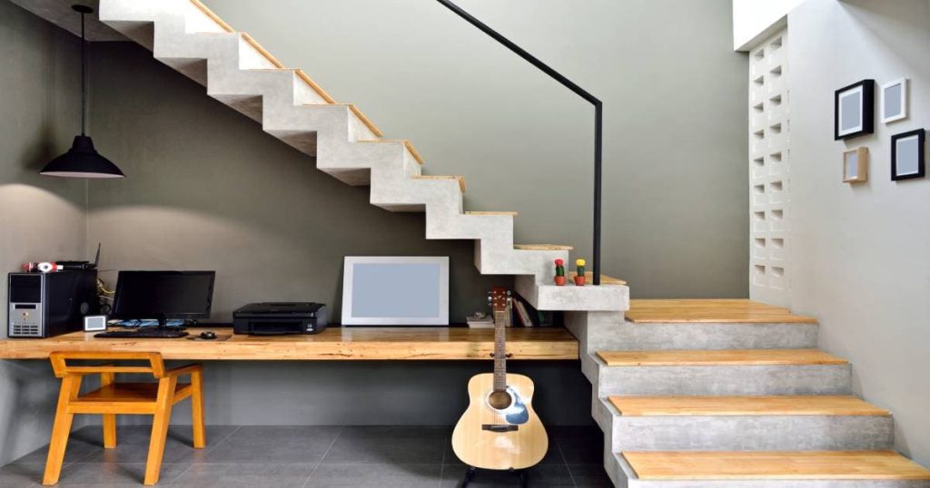Een betonnen trap met pvc trapcovers in houtlook. Onder de trap werd een bureautje ingericht met een houten tafel, houten bureaustoel, computer en klassieke gitaar.