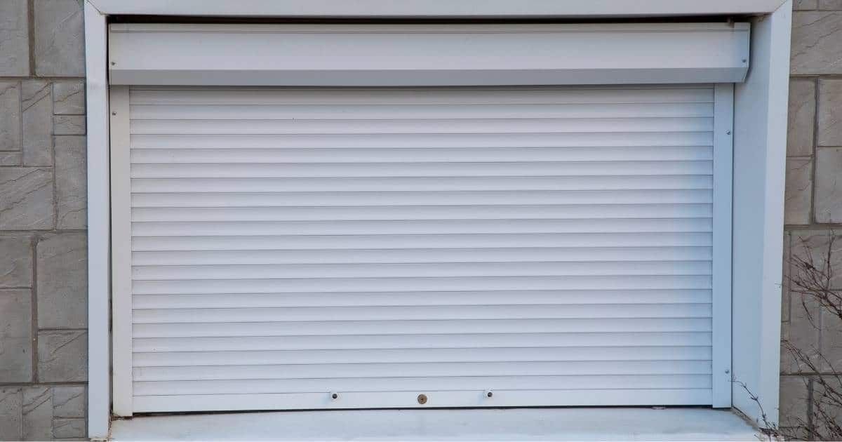 Een raam in een stenen gevel, voorzien van een inbraakwerend rolluik met slot, uitgevoerd in wit pvc.