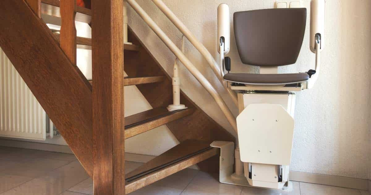Een klassieke stoellift of traplift op een houten molenaarstrap, tegen een crèmekleurige muur. 