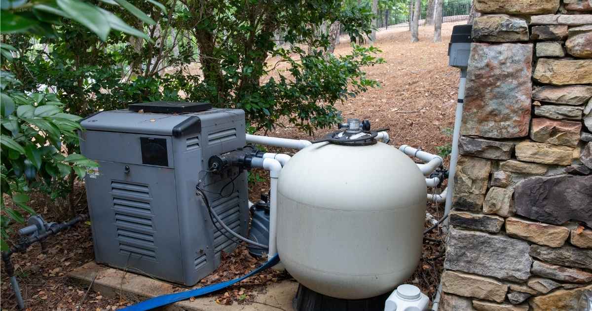 Een eenvoudig regenwatersysteem met drukvat en aanzuigende regenwaterpomp naast een woning met stenen gevel.