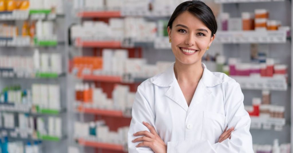 Een apotheker in witte jas staat voor rekken met medicatie.