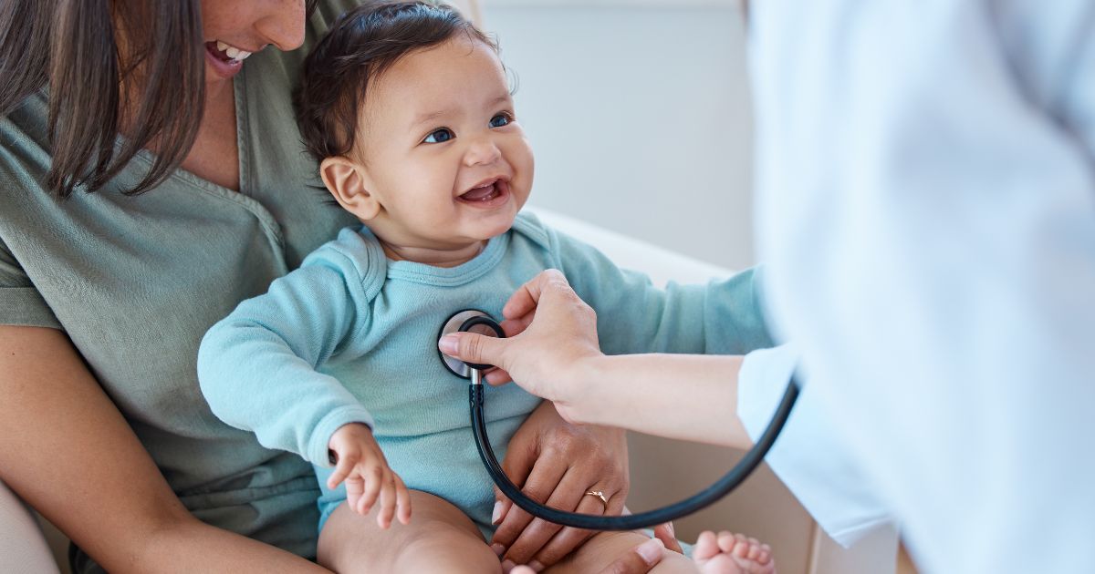 Een dokter onderzoekt een jong kind met een stethoscoop. Het kind zit bij een vrouw op de schoot.