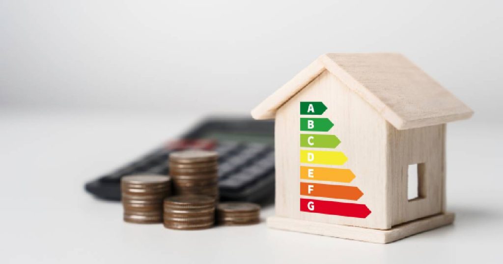 Een gunstig energielabel voor je woning bespaart je heel wat geld. Een houte huisje met de verschillende energielabels. Plus muntstukken en een rekentoestel op de achtergrond.