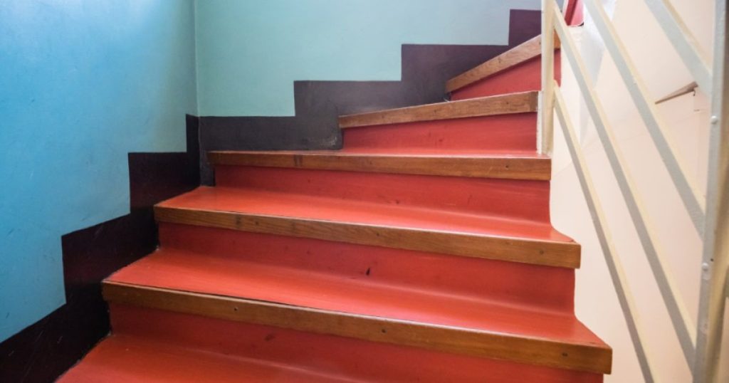 Trap in rode marmoleum met houten trapneuzen. Samen met de blauwe zijwand vormt de trap een mooie eclectische mix.