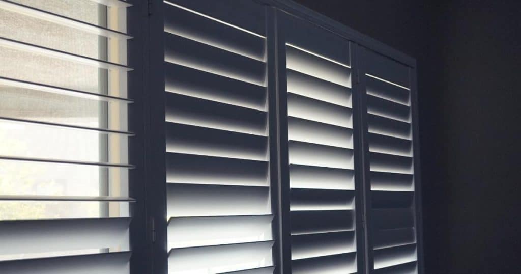 Een raam met stevige rolluiken met kantelbare lamellen in kunststof: een deel van de lamellen is open gekanteld, een deel is gesloten.