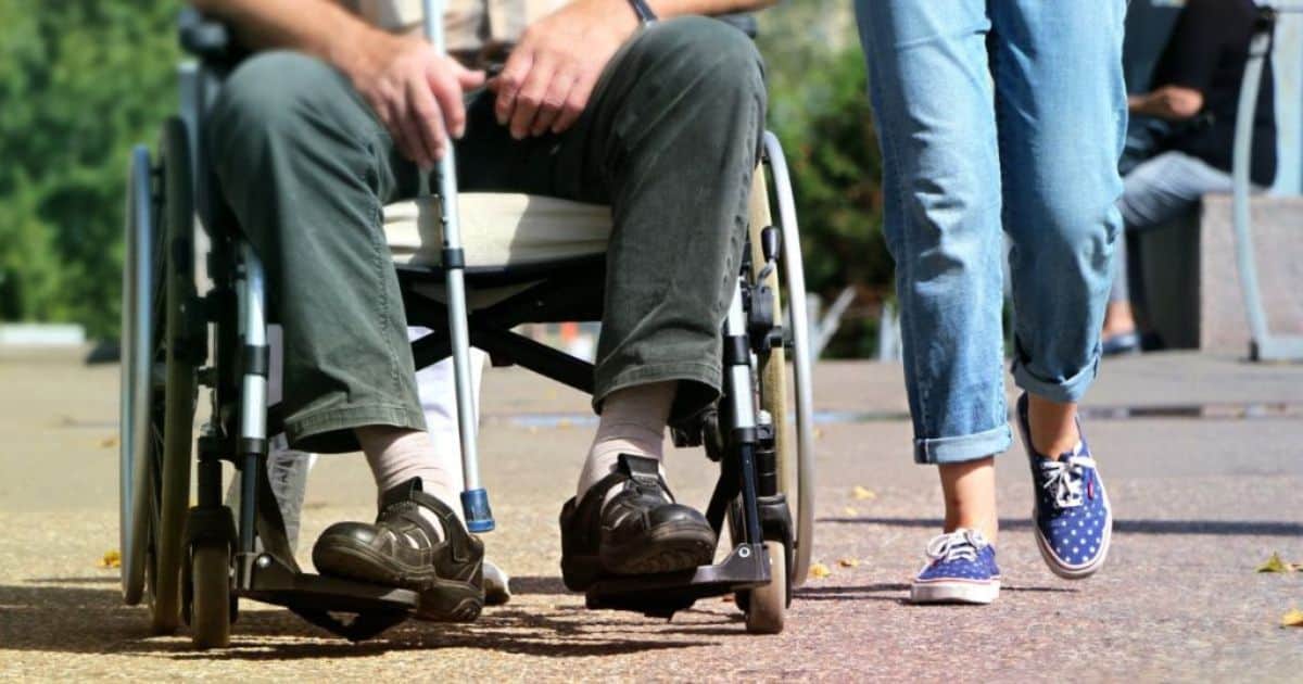 De benen van een man in een rolstoel naast de benen van een jong persoon in jeansbroek.