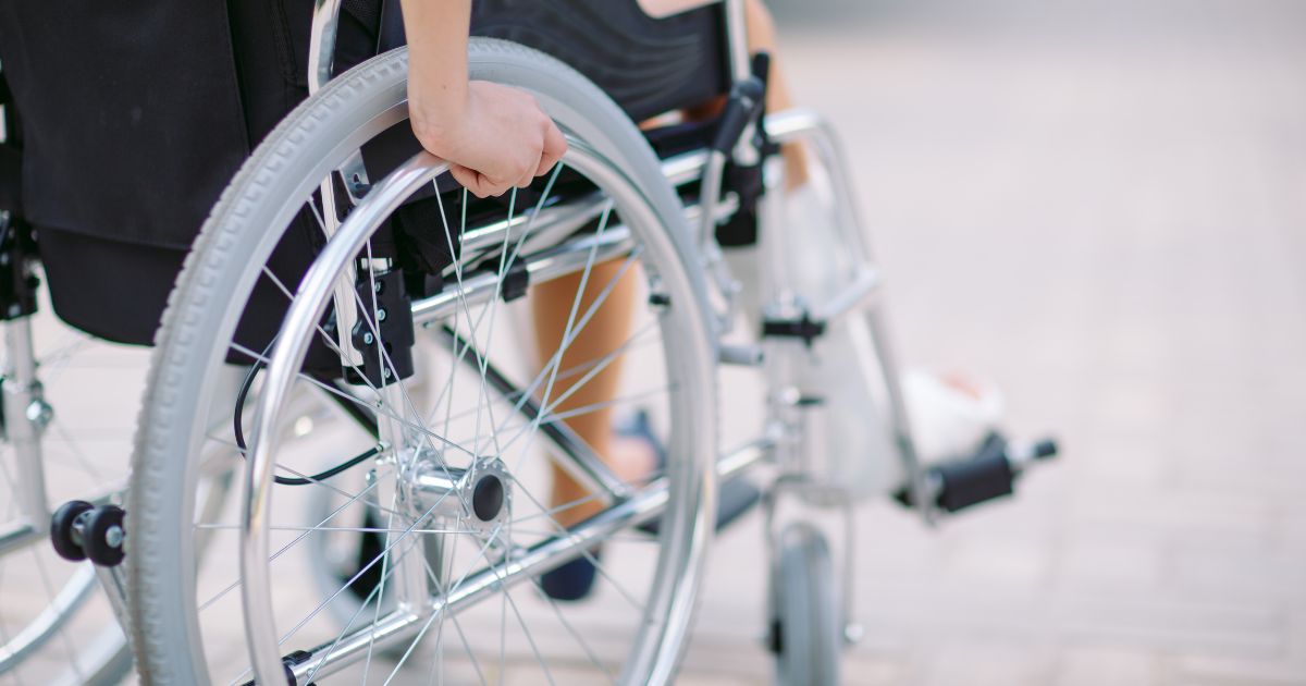 Close-up van het achterwiel van een uitgeleende rolstoel waarin een persoon met gebroken been zit.