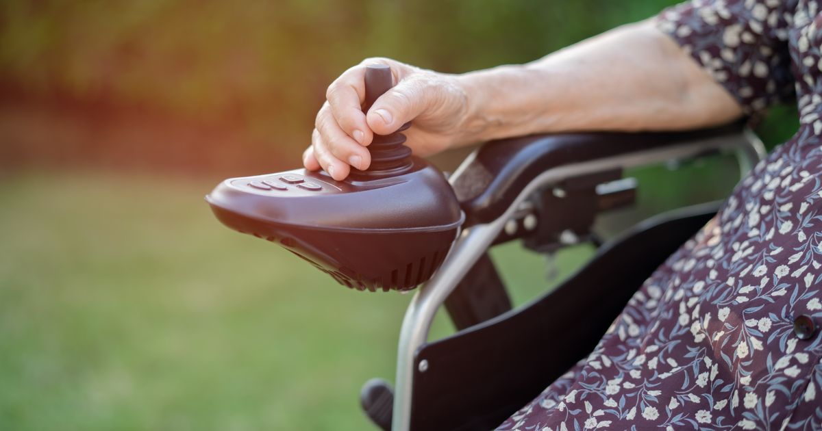 Close-up van een hand van een dame op het bedieningspaneel van een elektrische rolstoel.