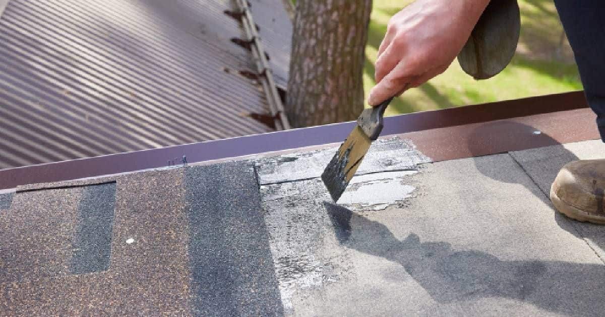 Een dakwerker gebruikt een vloeibaar product om een klein gaatje in oude roofing te herstellen.