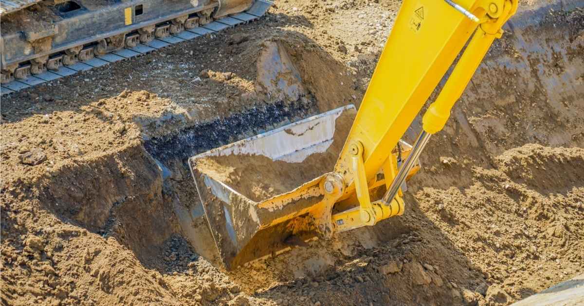 De scheplade van een gele rupskraan graaft een kuil om een terrein voor te bereiden op een nieuwbouwproject. 