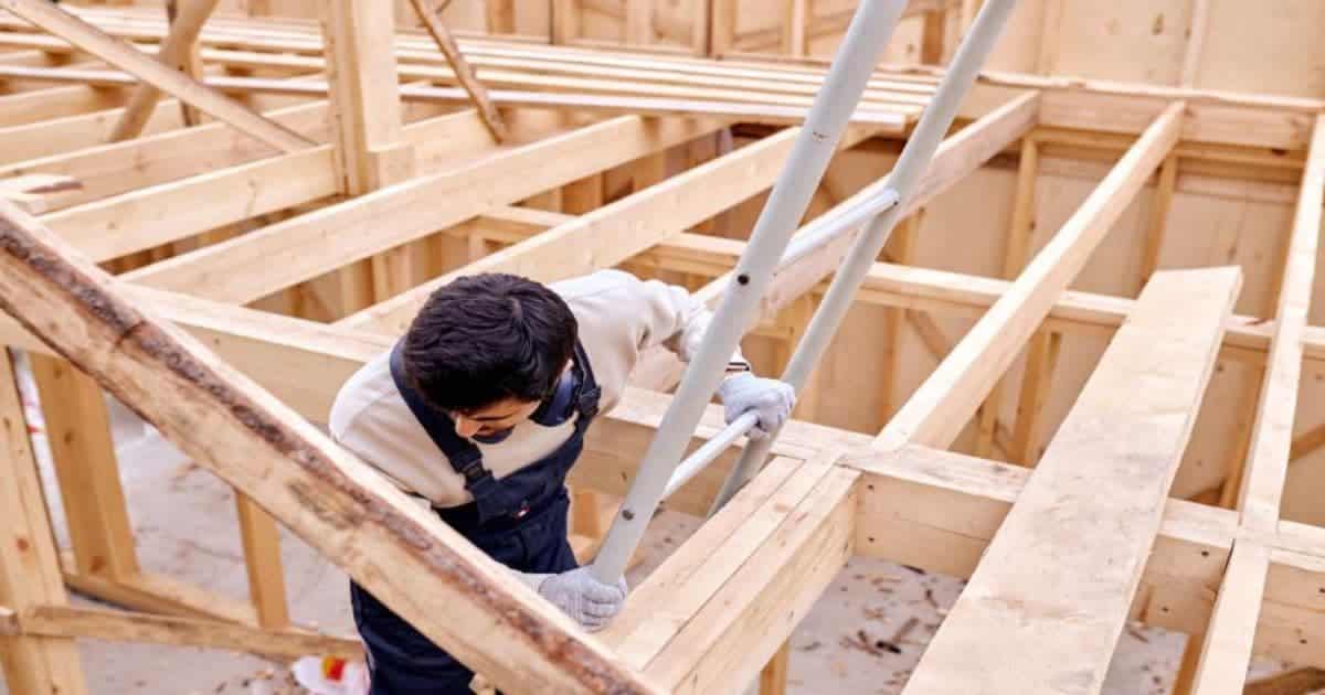 Arbeider plaatst houten draagstructuur tijdens de ruwbouwfase van een woning.