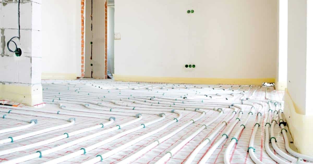 Een ruimte in een nieuwbouwwoning tijdens de ruwbouwfase. De muren zijn nog niet afgewerkt. Op de vloer liggen buizen voor vloerverwarming, die met kabelbinders vastgebonden zijn aan een mat.