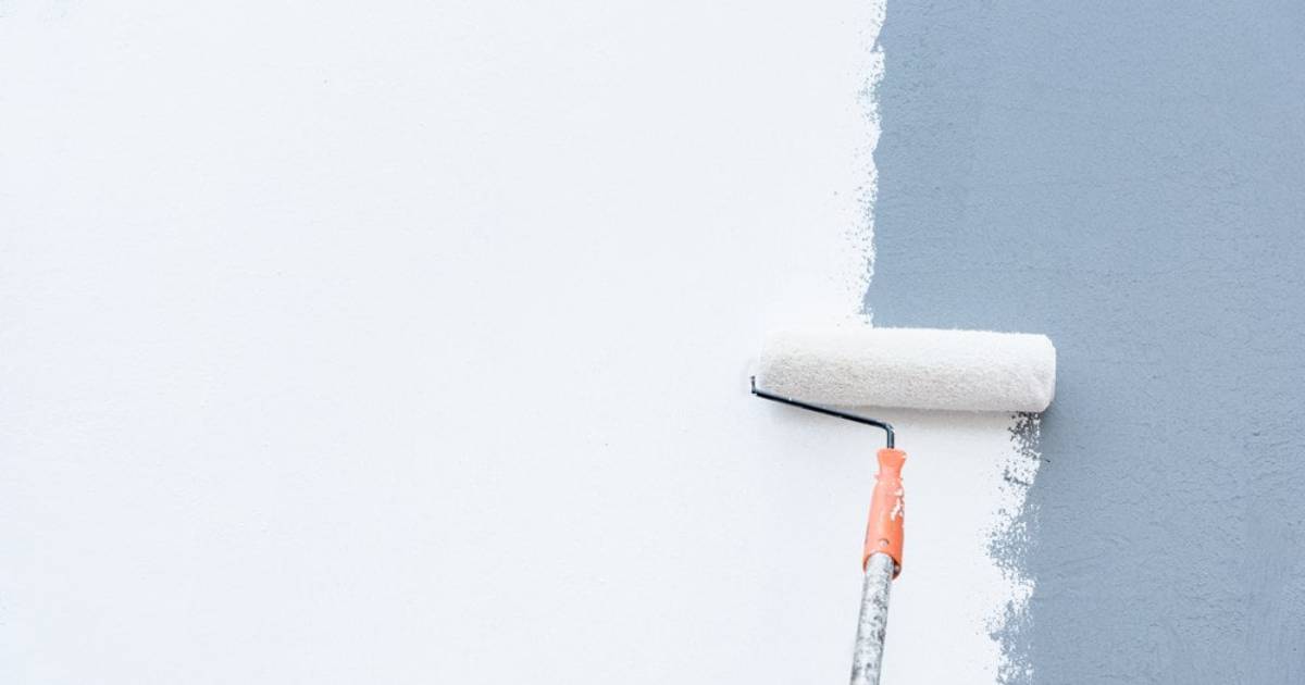 Met een verfroller wordt er een blauwe verflaag op een buitenmuur aangebracht.