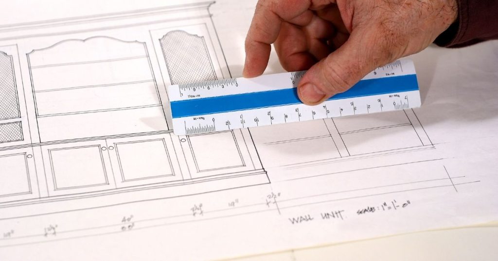 Een hand houdt een meetlat vast boven een wit blad met daarop het plan van een kast op maat.
