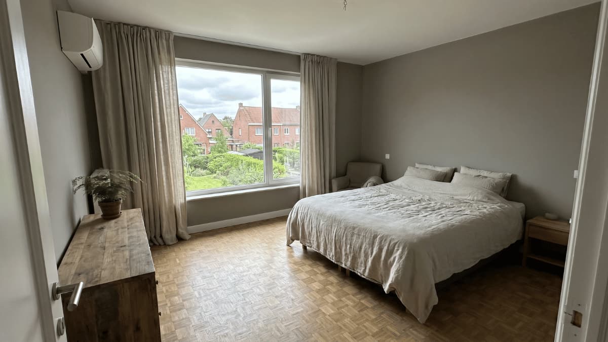 slaapkamer-met-airco-binnenunit-aan-de-muur-en-uitzicht-op-vlaamse-bakstenen-woningen.