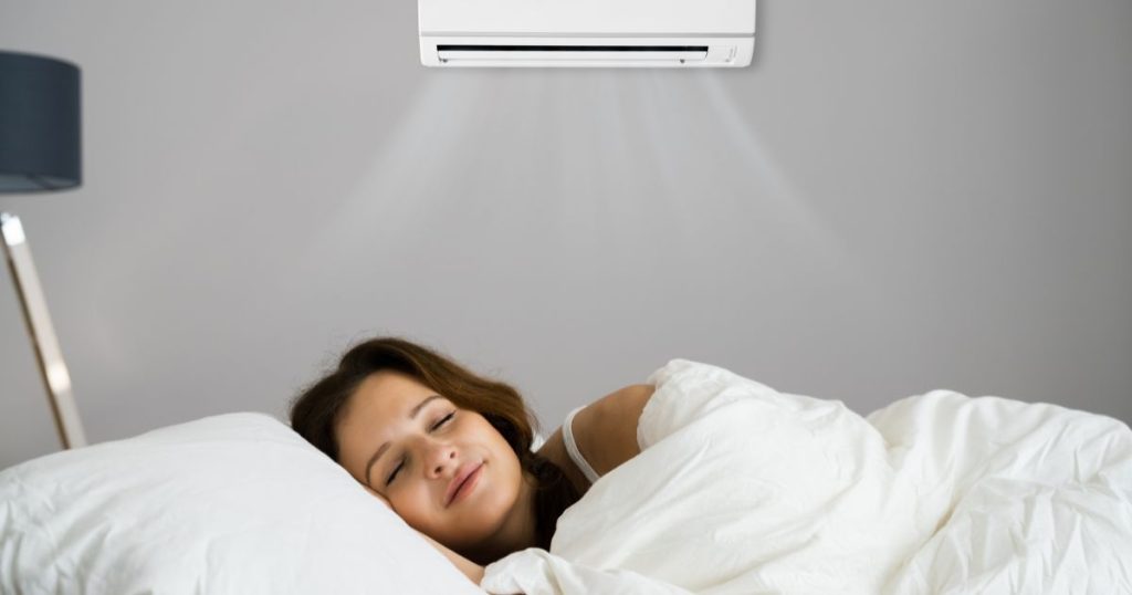 Een vrouw ligt vredig te slapen in een ruimte met een mobiele split airco die aan de wand bevestigd is. 