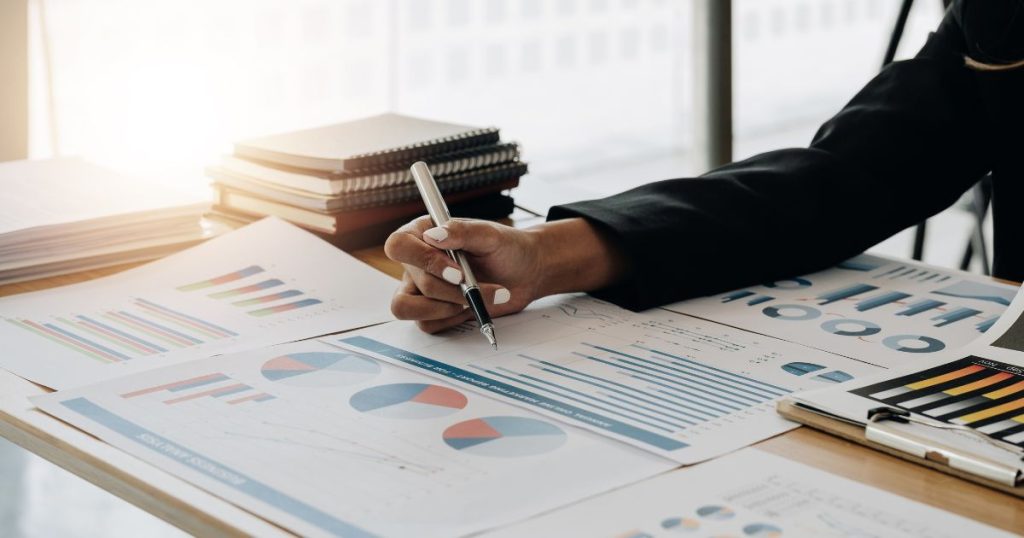Een dame houdt een pen vast boven verschillende papieren met grafieken die meer informatie bevatten over haar energieverbruik en de energieproductie van haar zonnepaneelinstallatie.