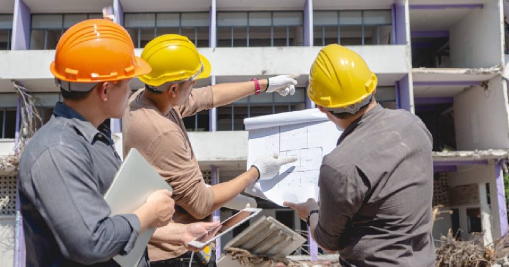 Drie bouwdeskundigen overlopen het sloopopvolgingsplan voor de ontmanteling van een oud appartementsgebouw.