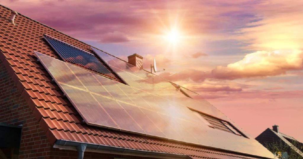 Een dak met zonnepanelen op een woning met een Smart Grid Ready warmtepompboiler. Op de achtergrond een prachtige zonsondergang.