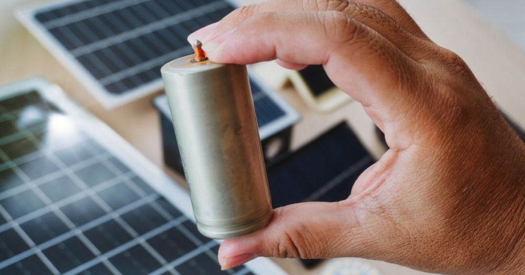 Een hand met een kleine batterij boven een collectie kleine zonnepanelen.