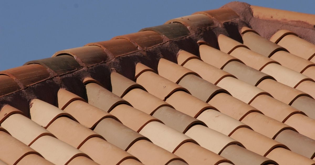 Close-up van de nok van een hellend dak, bedekt met holle keramische dakpannen in oranje tinten.