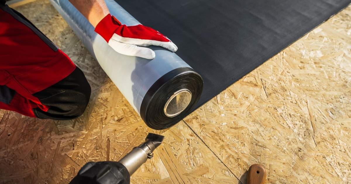 Een dakdekker lijmt een rol EPDM op het houten dakbeschot van een plat dak.