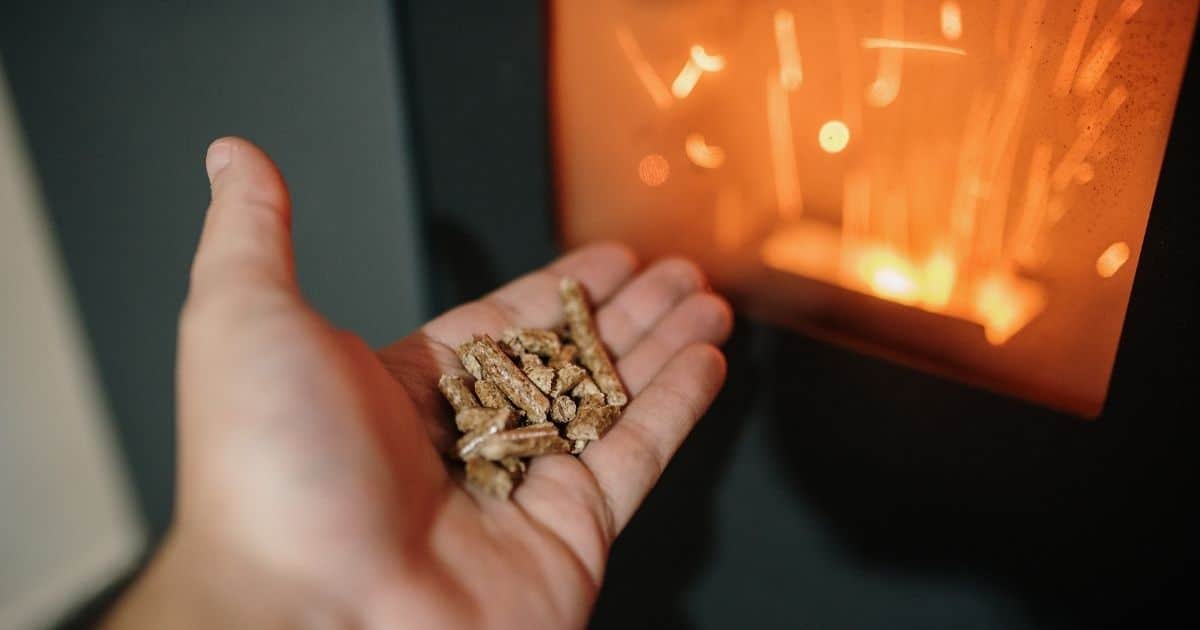 Een hand met pellets voor een brandende zwarte pelletkachel.